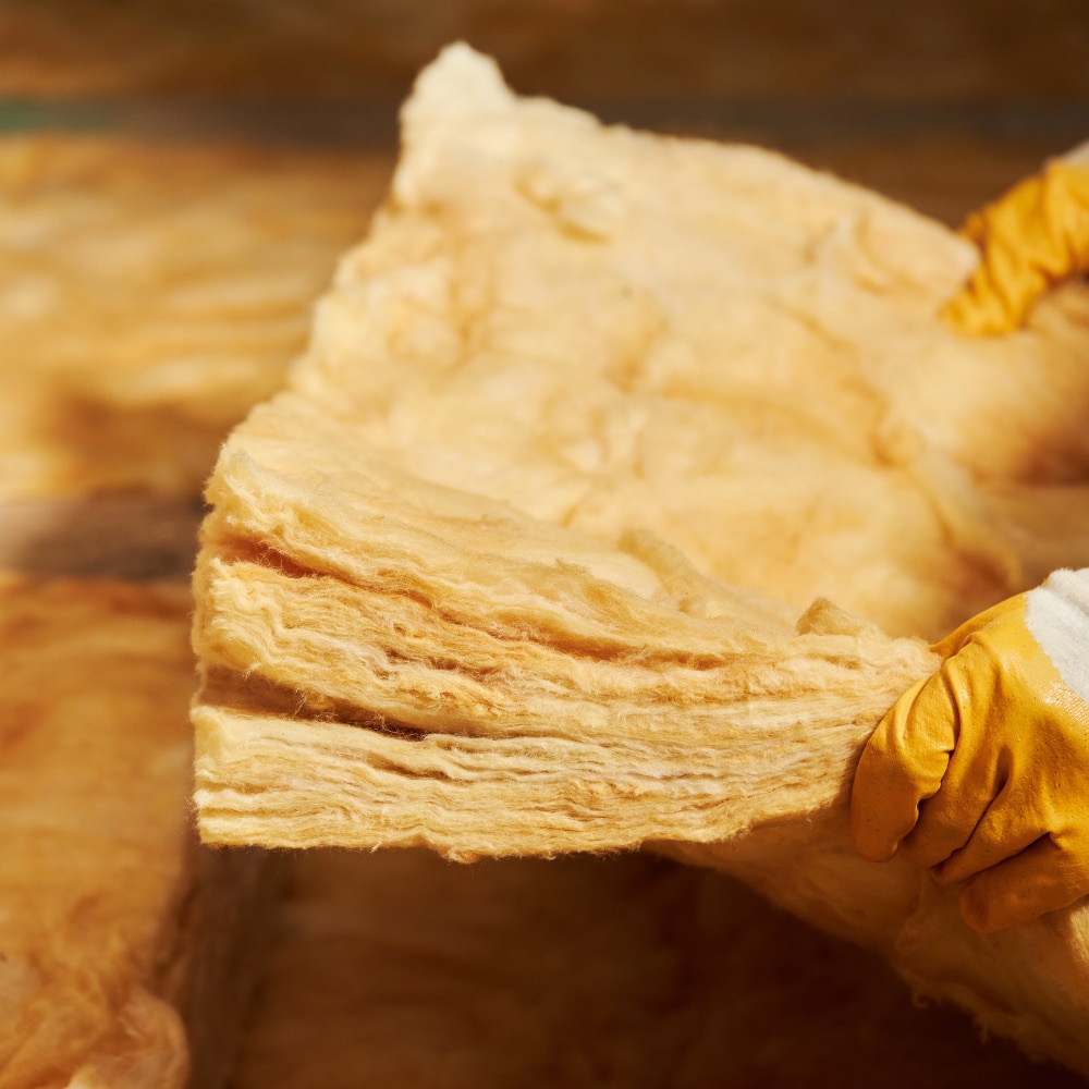 Mains gantées de jaune manipulant un épais panneau d'isolant thermique de couleur paille. Pose d'isolation en laine minérale.