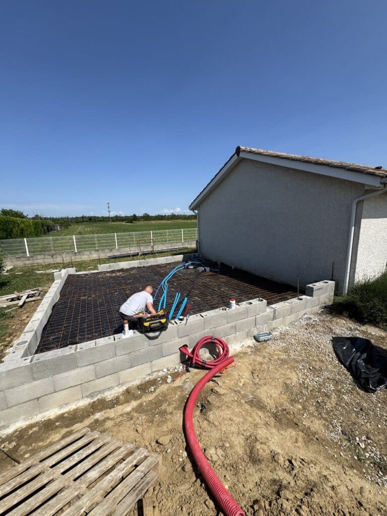 Ouvrier installant treillis et gaines pour fondations d'extension de maison sur chantier de construction.