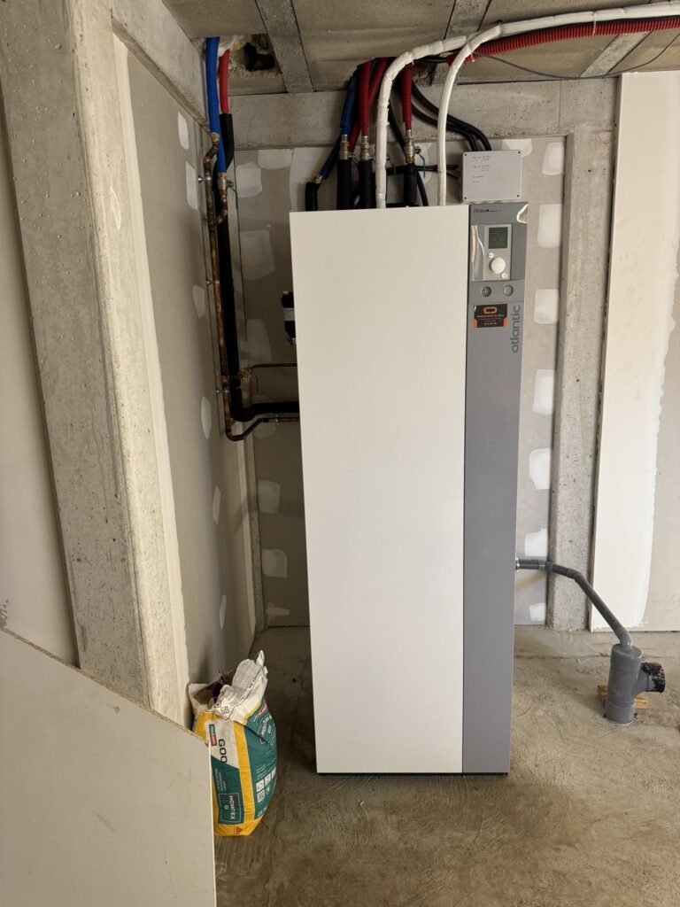 Pompe à chaleur Atlantic Alfea Excellia HP installée dans un local technique avec sa tuyauterie.