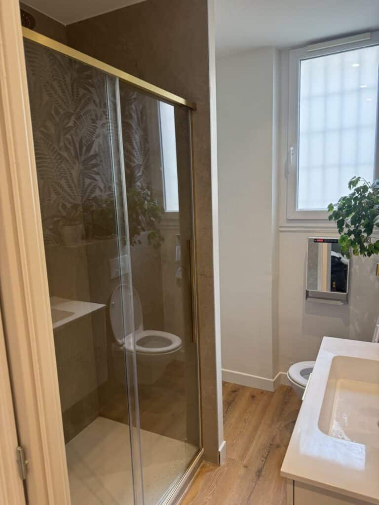 Petite salle de bain moderne avec douche et carrelage tropical Salle de bain moderne : douche à l'italienne, carrelage motif feuille, robinetterie dorée et sol aspect bois.